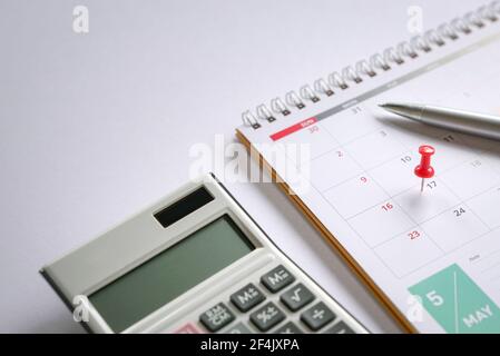 Red push pin on May 17 calendar with pen and calculator on top of table. Reminder of new tax day for 2021. Stock Photo