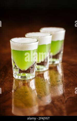 Three shot glasses of green alcoholic cocktails