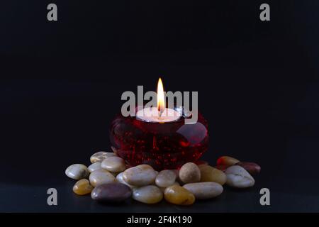 Mourning or prayer concept. Burning candle in a round red candlestick with colored stones surrounding it. All this on a black background. Stock Photo