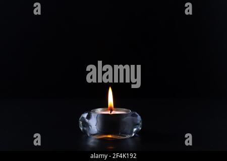 Mourning or prayer concept. Burning candle in a transparent round candlestick. Stock Photo