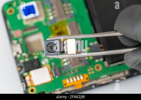 Fix the phone.A technician or master repairs a mobile phone, he installs and changes the camera in the motherboard. Hands, gloves, macro Stock Photo