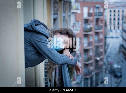 Beautiful depressed lonely woman with face mask in quarantine staring out on balcony feeling sad, lonely, pain and grief during coronavirus outbreak. Stock Photo