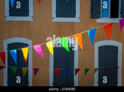 multi colour  celebration flags or bunting hanging in french street with colorful facade and shutters ,focus on flags . Stock Photo