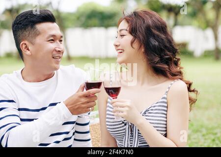Cheerful excited boyfrend and girlfriend toasting with wine glasses and looking at each other Stock Photo