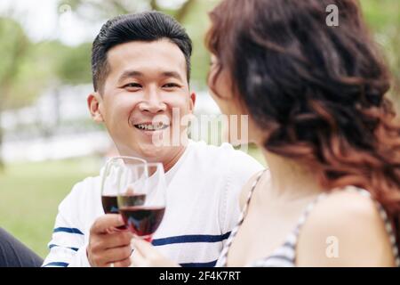 Portrait of smiling handsome young Asina man enjoying picnic with girlfriend and drinking wine Stock Photo