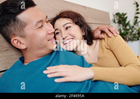 Happy pretty young woman lying on bed with boyfriend and looking at him with love and tender Stock Photo