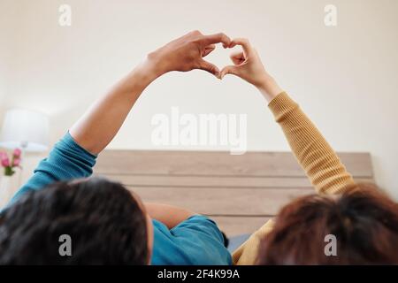 Young couple in love lying on bed and making heart gesture with fingers Stock Photo