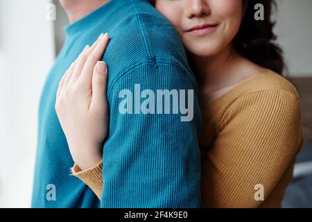 Cropped image of young woman in love hugging boyfriend from behind when they are standing by window Stock Photo