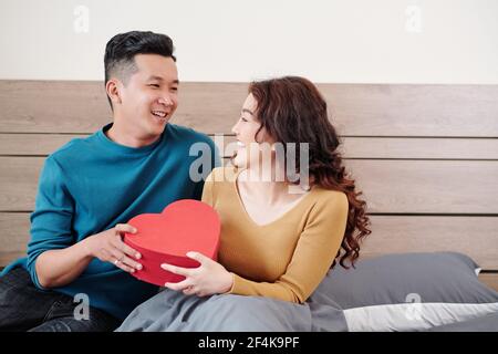 Happy young Vietnamese man giving Valentines day present to his smiling pretty girlfriend Stock Photo