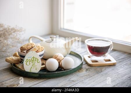 Homemade Easter still life with tea and cookies on the windowsill in the morning. Easter family holiday concept. Stock Photo