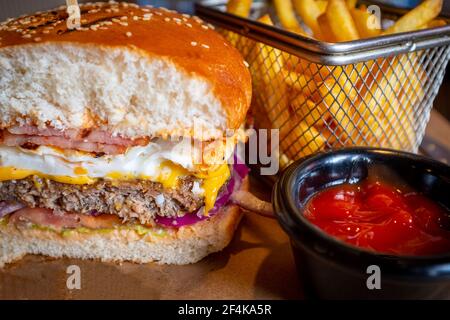 Home made tasty beef burger with egg, bacon, and chips with tomato sauce Stock Photo