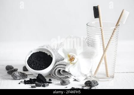 Still life with organic bamboo brushes and activated carbon powder and an orchid flower as a decorative element. Oral hygiene and dental care. Stock Photo