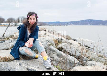 Peekskill, New York, USA. Portrait of a young, teenage gil sitting at a rocky pier at the Hudson River Shoreline. Stock Photo