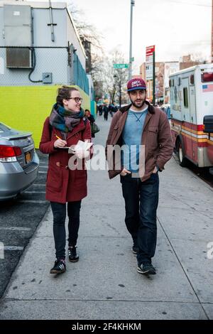 New York City, USA. Young urban male giving a tour through the Roosevelt Avenue neighborhood in Queens, to his brunette, female friend. Stock Photo