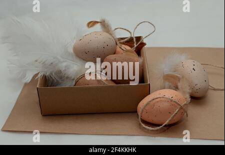 Brown easter eggs with white feathers in a cardboard box on a table Stock Photo