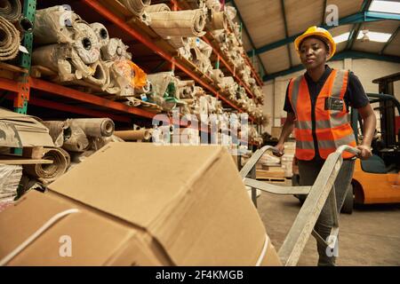 African female warehouse worker moving stock using a dolly Stock Photo