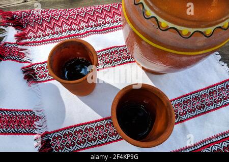 Kvass in clay glasses and jug on a wooden table with national textiles. Ukrainian authenticity national style Stock Photo