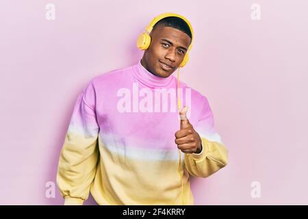 Young black man listening to music wearing headphones doing happy thumbs up gesture with hand. approving expression looking at the camera showing succ Stock Photo