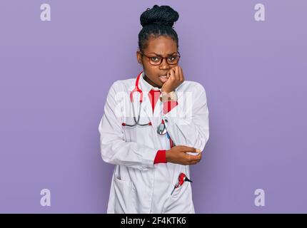 Young african american woman wearing doctor uniform and stethoscope looking stressed and nervous with hands on mouth biting nails. anxiety problem. Stock Photo