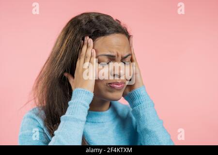 Portrait of african woman having headache, pink studio portrait. Girl putting hands on head. Concept of migraine problems, medicine, illness Stock Photo