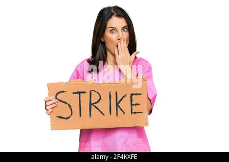 Middle age brunette doctor woman holding strike banner cardboard covering mouth with hand, shocked and afraid for mistake. surprised expression Stock Photo
