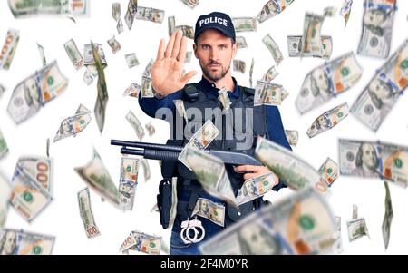 Young handsome man wearing police uniform holding shotgun stressed and frustrated with hand on head, surprised and angry face Stock Photo