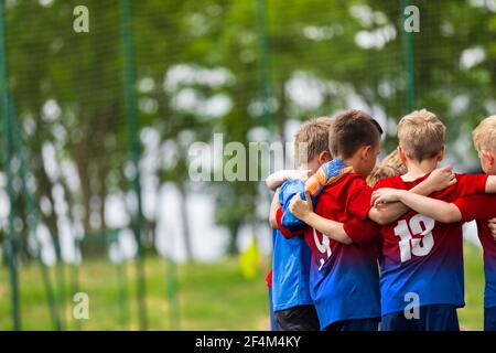 Happy Children Huddling in a Team on Sports Field. Group of School Boys Standing Together in a Circle and Motivating Themselves Before Football Match Stock Photo