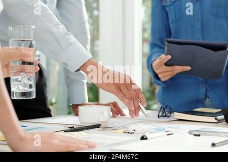 Hands of financial analyst pointing at chart on table in meeting room when talking to marketing department managers Stock Photo