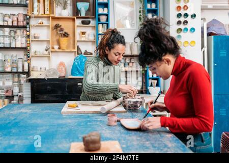 Stock photo of two happy women in apron using clay during pottery class. Stock Photo