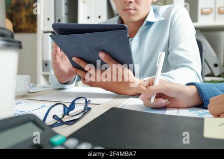 Serious entrepreneur reading data on digital tablet when his coworker analyzing report, selective focus Stock Photo