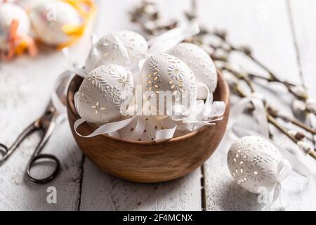 Handmade white easter eggs with willow catkins in a wooden bowl on wooden table. Stock Photo
