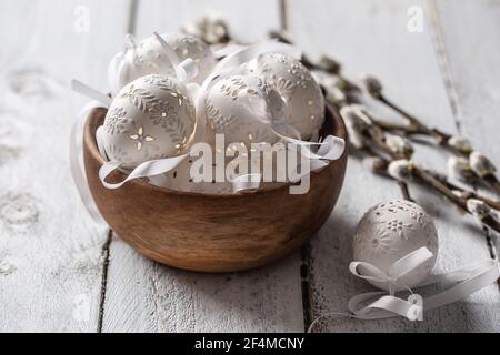 Handmade white easter eggs with willow catkins in a wooden bowl on wooden table. Stock Photo