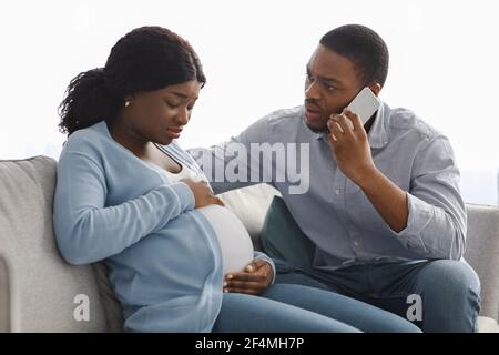 Worried black man calling doctor while wife having laibor pains Stock Photo