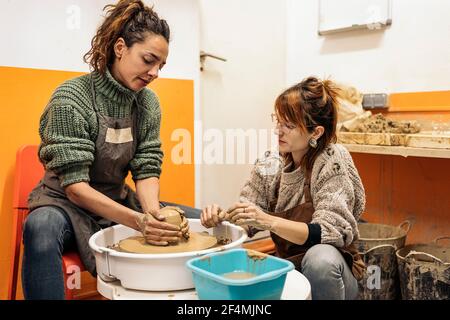 Stock photo of pottery teacher explaining to concentrated woman how to use spinning wheel. Stock Photo