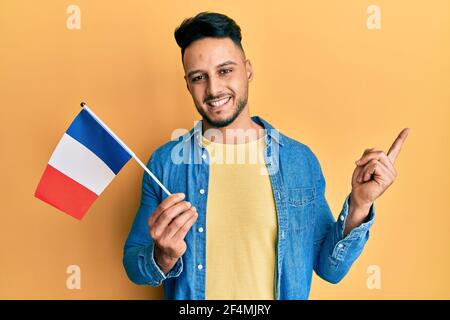 Young arab man holding france flag smiling happy pointing with hand and finger to the side Stock Photo