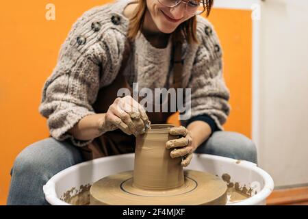 Stock photo of concentrated woman in apron working behind a potter's wheel in a workshop. Stock Photo