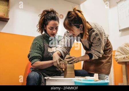 Stock photo of pottery teacher explaining to concentrated woman how to use spinning wheel. Stock Photo