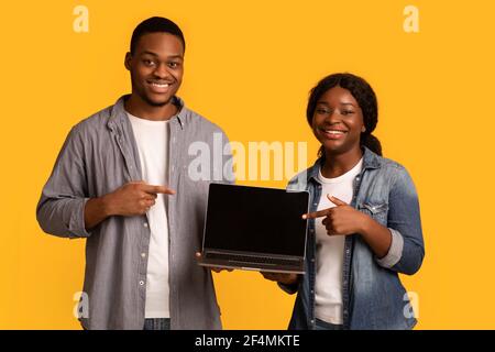 Check This Website. Smiling black couple pointing at laptop with blank screen Stock Photo