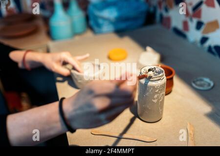 Stock photo of unrecognized woman using paintbrush during her pottery class.