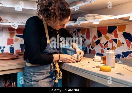Stock photo of concentrated woman in apron working in pottery atelier. Stock Photo
