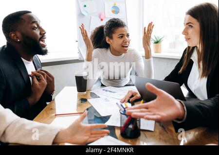 Emotional young adult people having a conflict on business meeting. Worried multiethnic colleagues can't make a deal or come to agreement, arguing, failed project concept Stock Photo