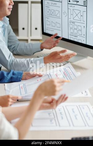 Group of UI and UX designers discussing project layouts at meeting when working on new mobile application Stock Photo
