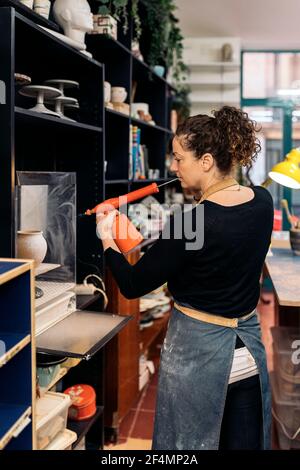 Stock photo of happy woman in apron working in pottery atelier.