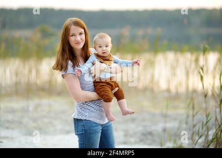 Cute little baby boy in his mothers arms. Mom and son having fun on sunny summer day in city park. Adorable son being held by his mommy. Stock Photo