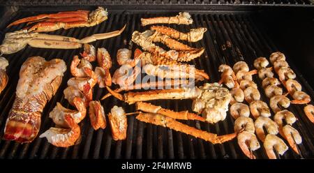 A collection of different kinds of seafood bbq cooking on a grill with lobster tail that is saddleback, tiger shrimp, shrimp on skewers, Alaskan snow Stock Photo