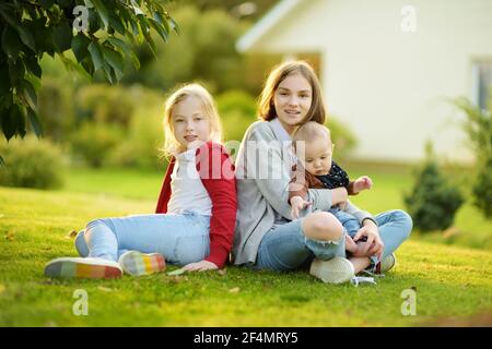 Two big sisters and their infant brother having fun outdoors. Two young girls holding their baby boy sibling on summer day. Kids with large age gap. B Stock Photo