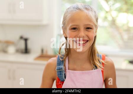 Portrait of smiling caucasian girl wearing apron standing in kitchen Stock Photo