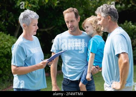 Caucasian senior couple with clipboard and father carrying son in volunteer shirts talking in field Stock Photo