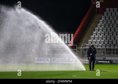 Groundsman ventilating football pitch standing beside sprinkler at lower league football stadium. Stock Photo