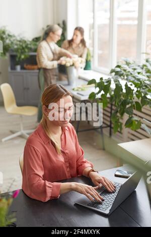 High angle view of young businesswoman using laptop in flower shop while managing small business, copy space Stock Photo